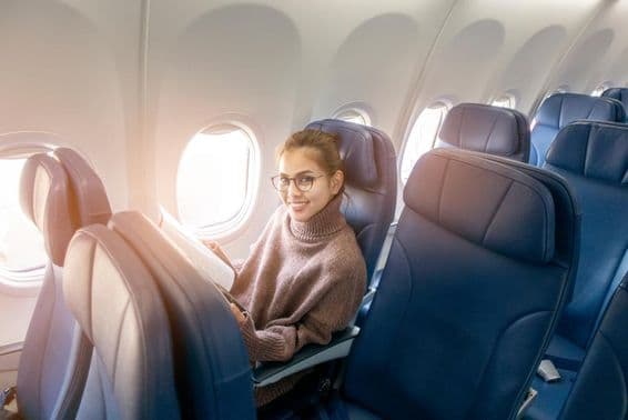 एक विमान में पत्रिका पढ़ती एशियाई महिला।