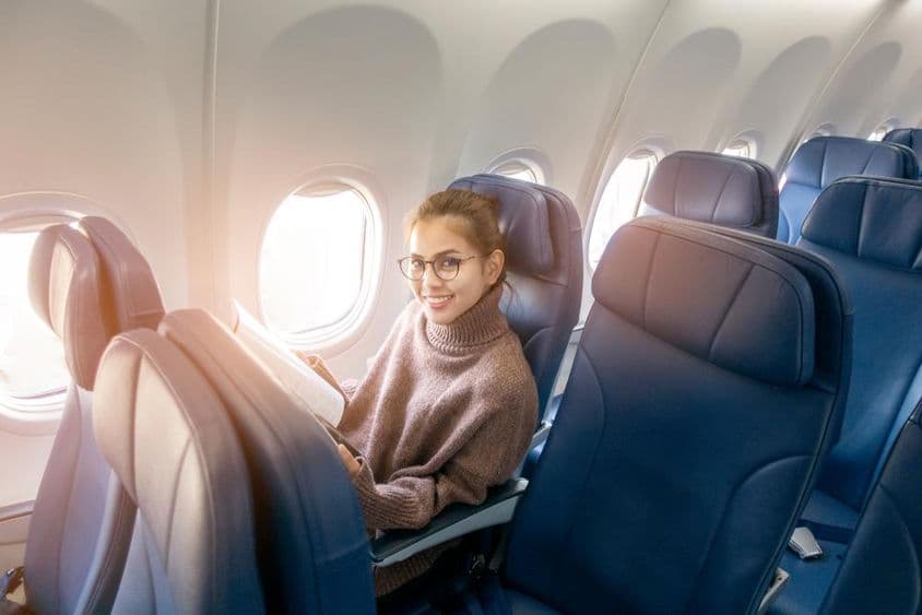 एक विमान में पत्रिका पढ़ती एशियाई महिला।