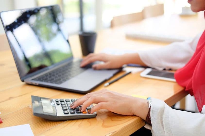 दुबई में एक महिला कर्मचारी कैलकुलेटर के साथ वित्तीय डेटा की गणना कर रही है।