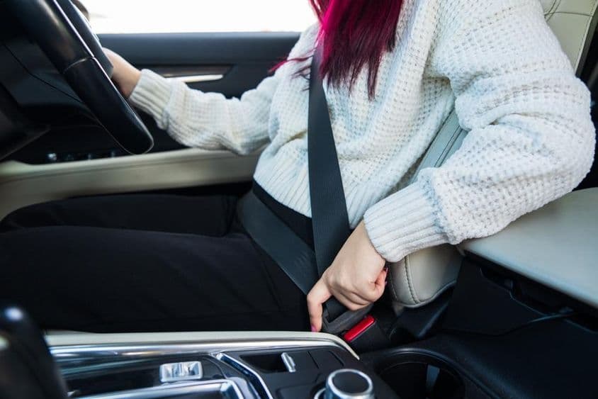 महिला ड्राइवर अपनी सीटबेल्ट बांध रही है।