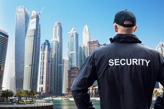 एक पुरुष सुरक्षा गार्ड शहर के दृश्य को पीछे से देखते हुए।