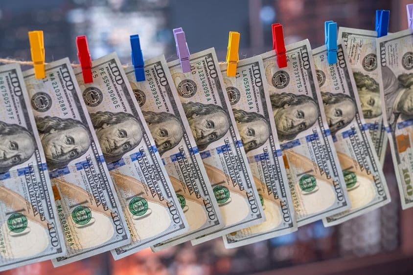 एक 100 अमेरिकी डॉलर का नोट लकड़ी के क्लिप के साथ कपड़े की रेखा पर लटका हुआ।