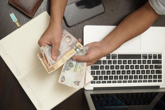 एक आदमी संयुक्त अरब अमीरात के दिरहम बैंकनोट की गड्डी गिन रहा है।