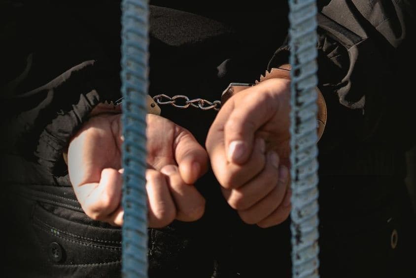 पुलिस स्टेशन में सलाखों के पीछे हथकड़ी पहने एक व्यक्ति।