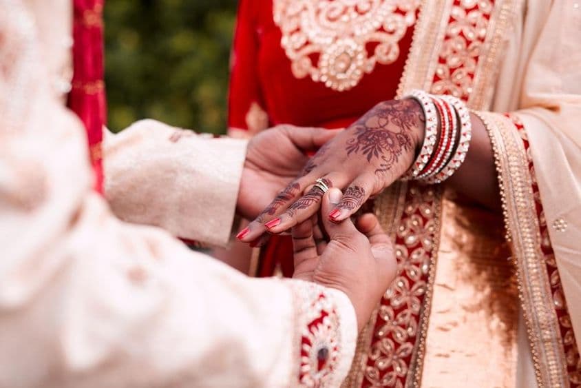 एक भारतीय दुल्हन के हाथ में अंगूठी पहना रही है।