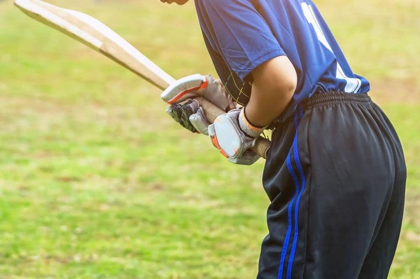 सुरक्षात्मक गियर में एशियाई युवा महिला क्रिकेटर क्षेत्र पर बल्ले से गेंद को मारते हुए।