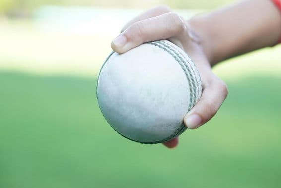 एक क्रिकेटर सफेद लेदर क्रिकेट गेंद को पकड़े हुए।
