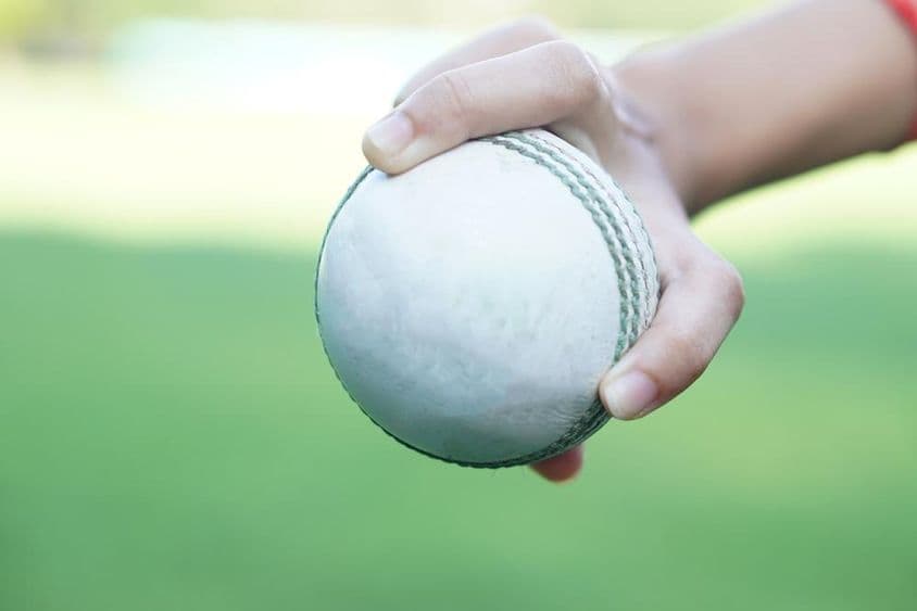 एक क्रिकेटर सफेद लेदर क्रिकेट गेंद को पकड़े हुए।
