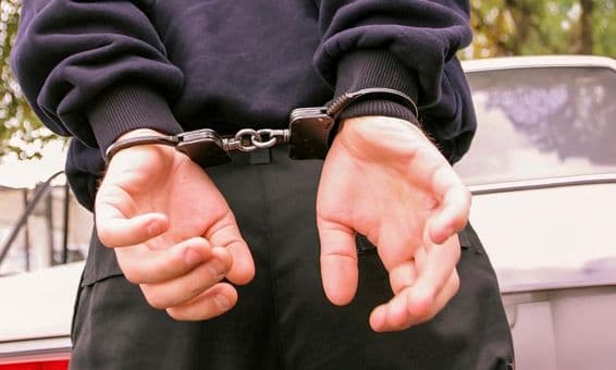 एक व्यक्ति जो अपनी पीठ के पीछे हथकड़ी वाले हाथ के साथ।