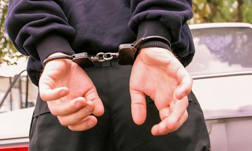 एक व्यक्ति जो अपनी पीठ के पीछे हथकड़ी वाले हाथ के साथ।