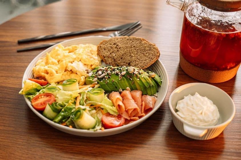 अंडे, एवोकाडो, हरी पत्तियाँ, सलाद और रास्पबेरी चाय के साथ स्वस्थ नाश्ता।