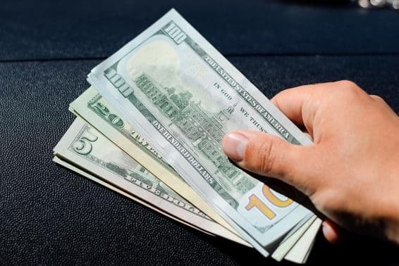 एक आदमी के हाथ में डॉलर का बंडल।