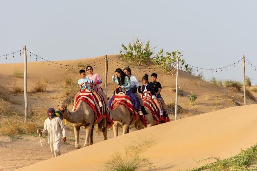 रेगिस्तान में ऊंट की सवारी करते हुए पर्यटक।
