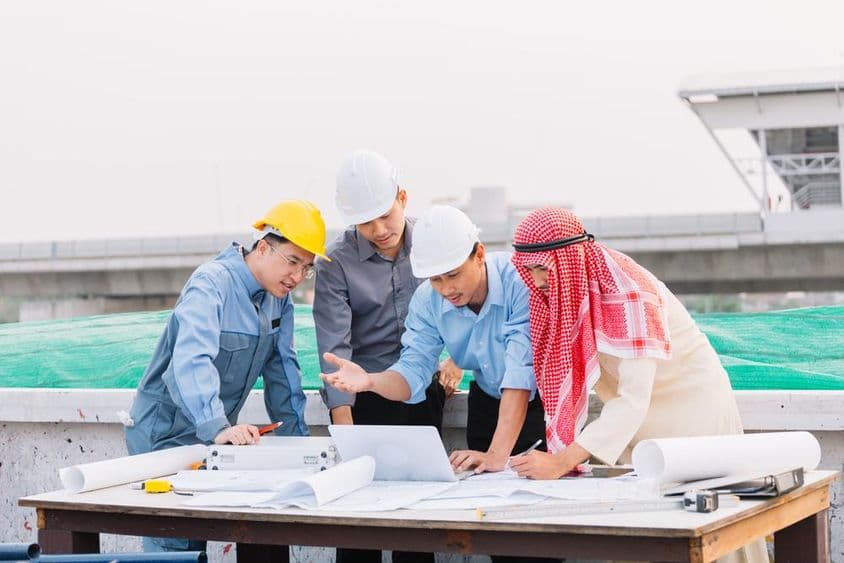 अरब व्यापारी, इंजीनियर, और श्रमिक निर्माण योजनाओं के साथ लैपटॉप का उपयोग करते हुए