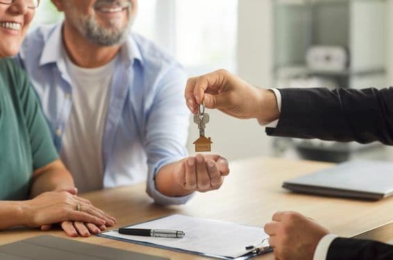 एक रियल एस्टेट एजेंट मुस्कुराते हुए बुजुर्ग दंपति को चाबियाँ सौंपते हुए।