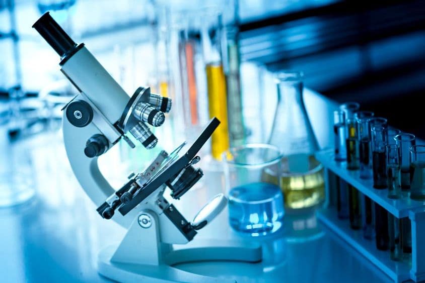 तालिका पर माइक्रोस्कोप के साथ रासायनिक ट्यूब और कांच के बर्तन।