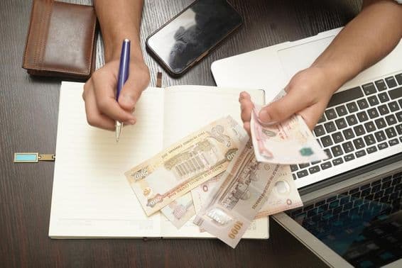 संयुक्त अरब अमीरात के दिरहम बैंकनोटों की गड्डी गिनता हुआ एक व्यक्ति।