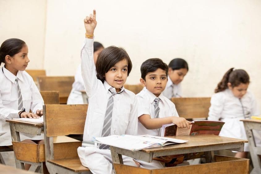 खुश भारतीय स्कूल बच्चा हाथ उठाता हुआ